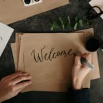 Handwriting a welcome card with calligraphy on craft paper, surrounded by art supplies.