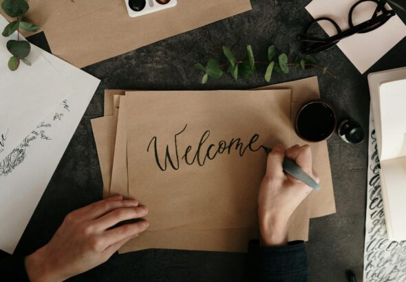 Handwriting a welcome card with calligraphy on craft paper, surrounded by art supplies.