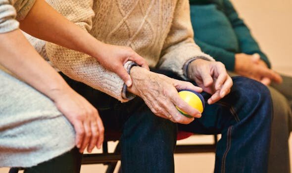 An elderly person receives support from a caregiver, holding hands indoors, showcasing compassion.